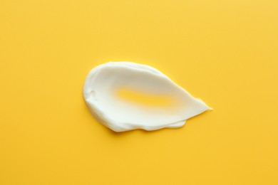 Photo of Sample of face cream on yellow background, top view