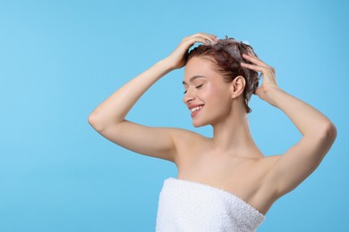 Photo of Happy young woman washing her hair with shampoo on light blue background