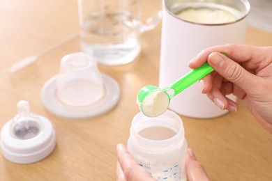 Photo of Woman preparing infant formula at table, closeup. Baby milk