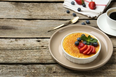 Delicious creme brulee with berries and mint in bowl on wooden table. Space for text