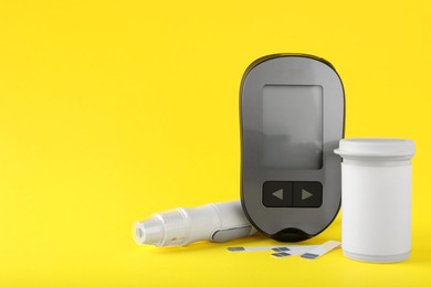 Photo of Digital glucometer, lancet pen, container and test strips on yellow background, space for text. Diabetes control