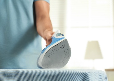 Handsome man ironing clean laundry at home, closeup