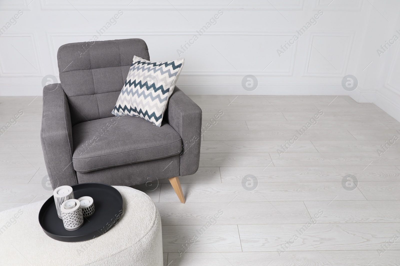 Photo of Stylish grey armchair and pouf with candles in room. Interior design