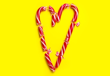 Photo of Heart made of crushed Christmas candy canes on yellow background, flat lay