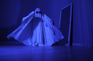 Photo of Creepy ghost. Woman covered with sheet in blue light