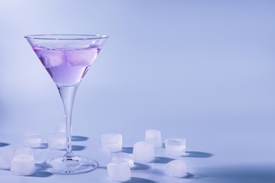 Photo of Martini glass with delicious cocktail and ice cubes on light blue background, space for text
