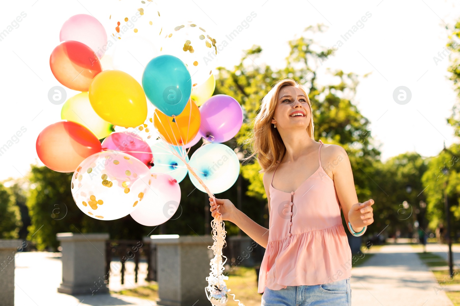 Photo of Young woman with colorful balloons outdoors on sunny day