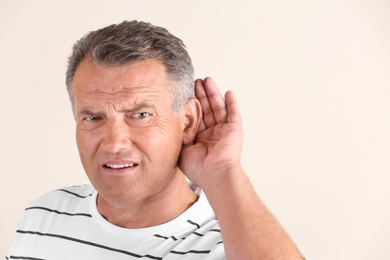 Mature man with hearing problem on light background