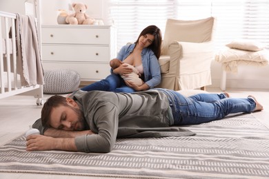 Tired young parents with their baby sleeping on floor in children's room