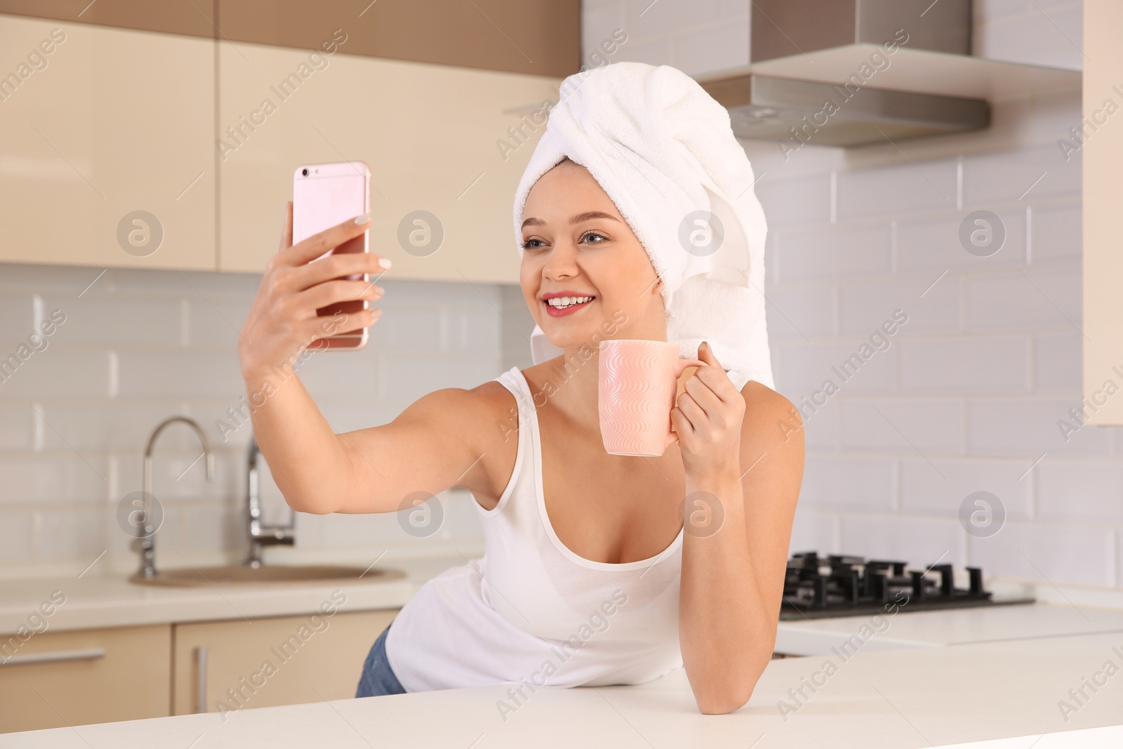 Photo of Beautiful woman with towel on head taking selfie in kitchen