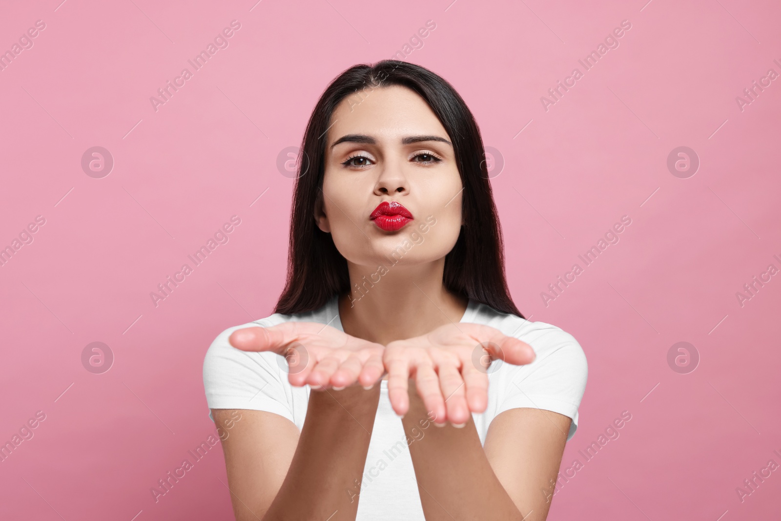 Photo of Beautiful young woman blowing kiss on pink background