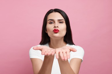 Photo of Beautiful young woman blowing kiss on pink background