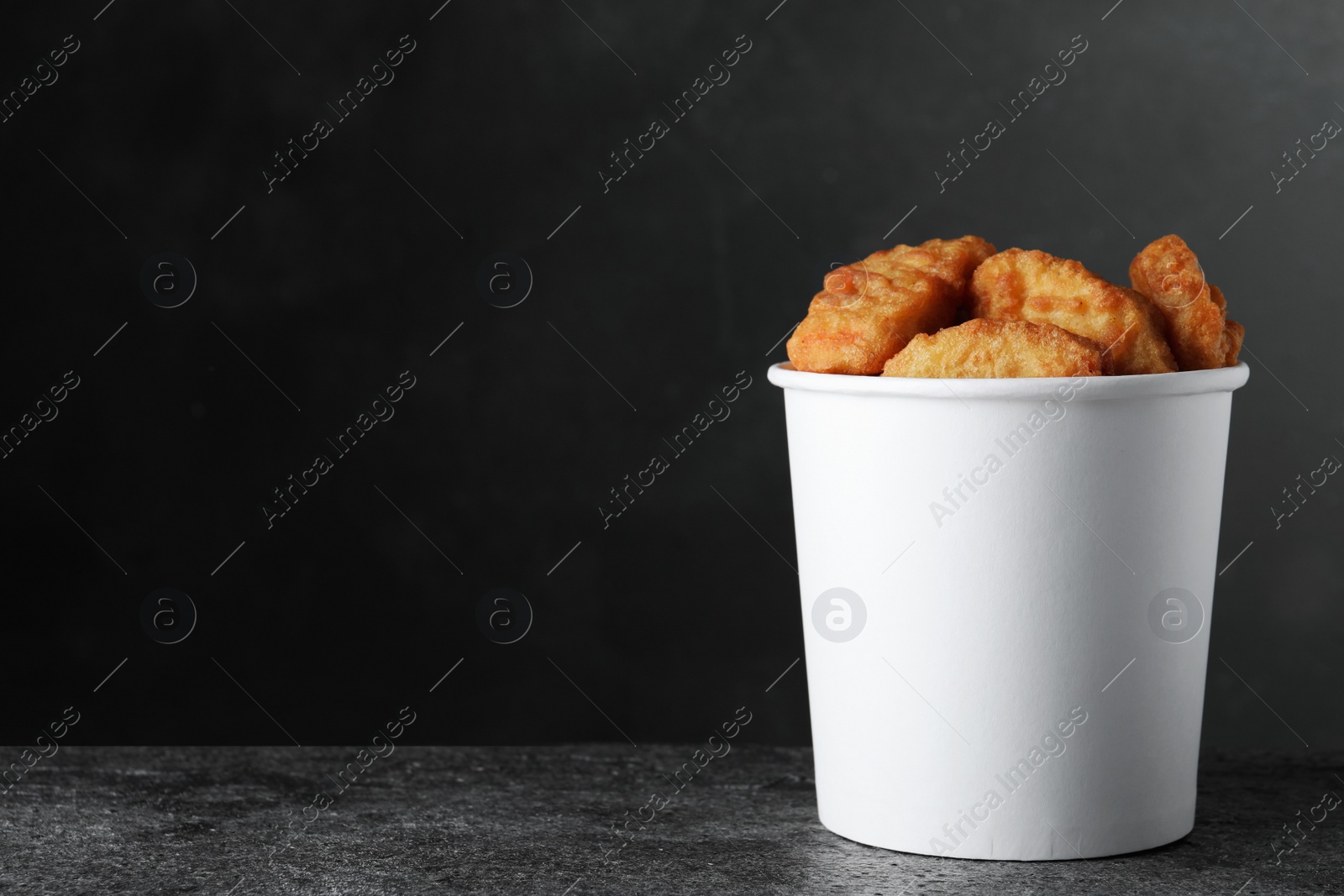 Photo of Bucket with delicious chicken nuggets on grey background. Space for text