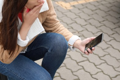 Photo of Woman holding damaged smartphone outdoors, closeup. Device repairing