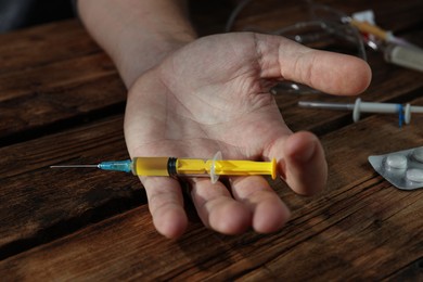 Drug addiction. Man with syringe on wooden table, closeup