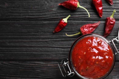 Jar of chili sauce and pepper on wooden table, flat lay. Space for text