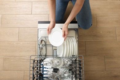 Photo of Woman loading dishwasher with glasses and plates, top view