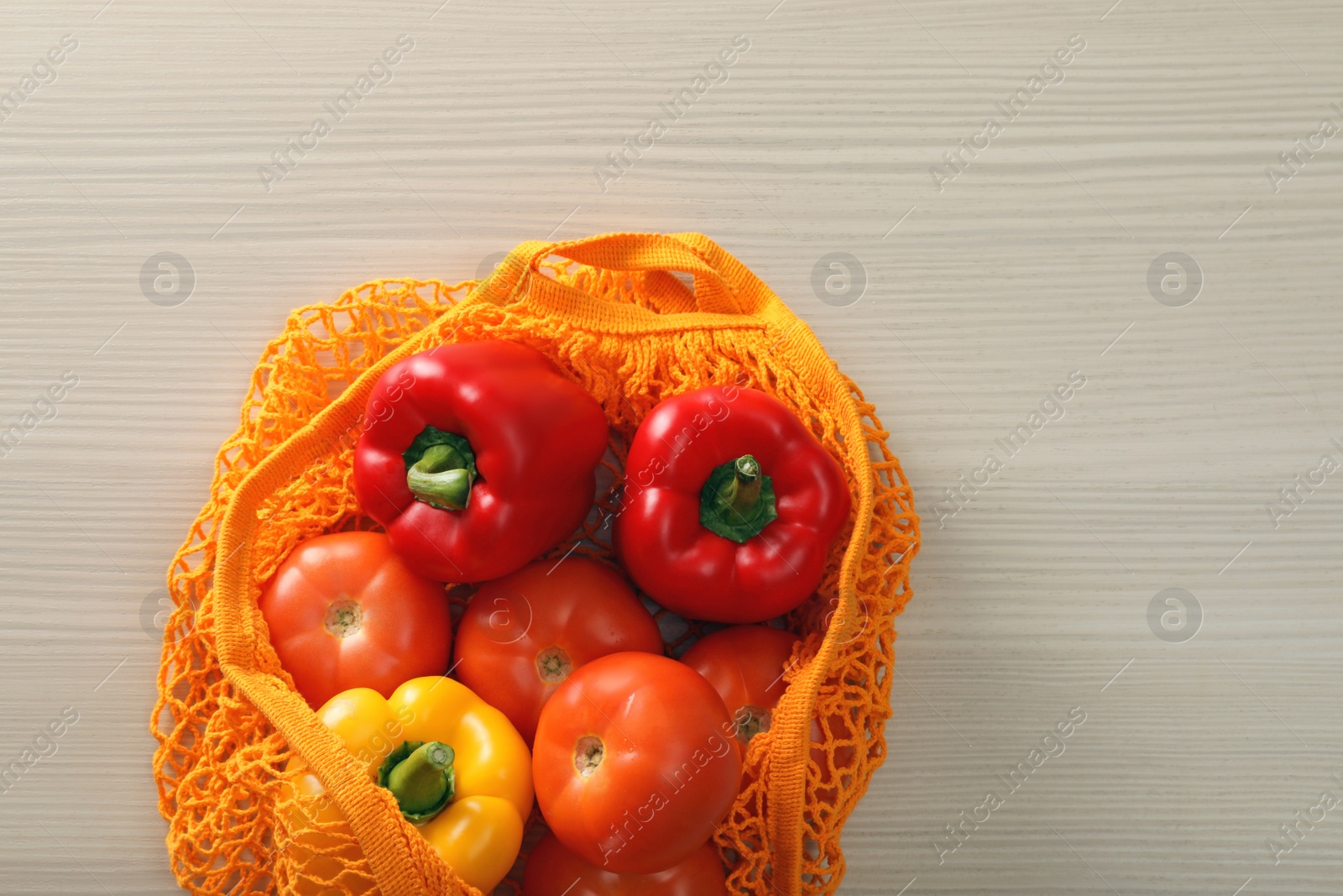 Photo of Net bag with vegetables on wooden table, top view