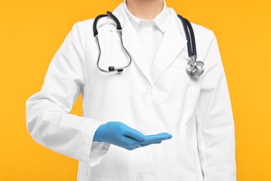 Photo of Doctor with stethoscope holding something on orange background, closeup