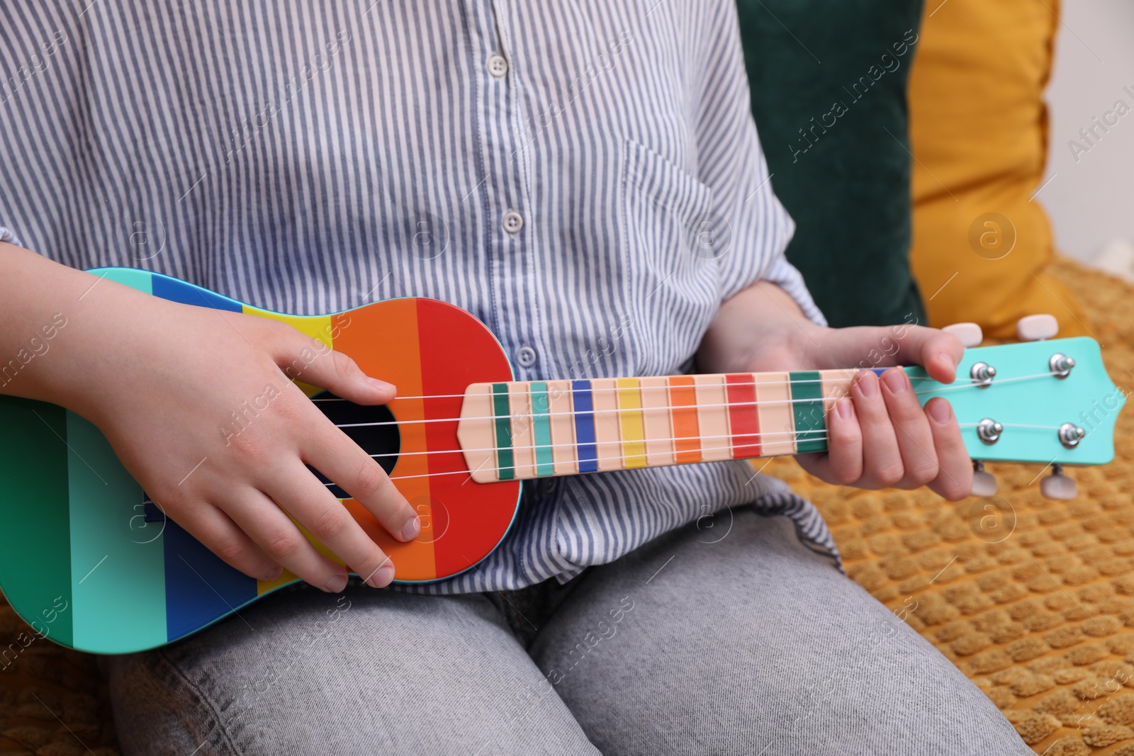 Photo of Woman playing ukulele on sofa at home, closeup