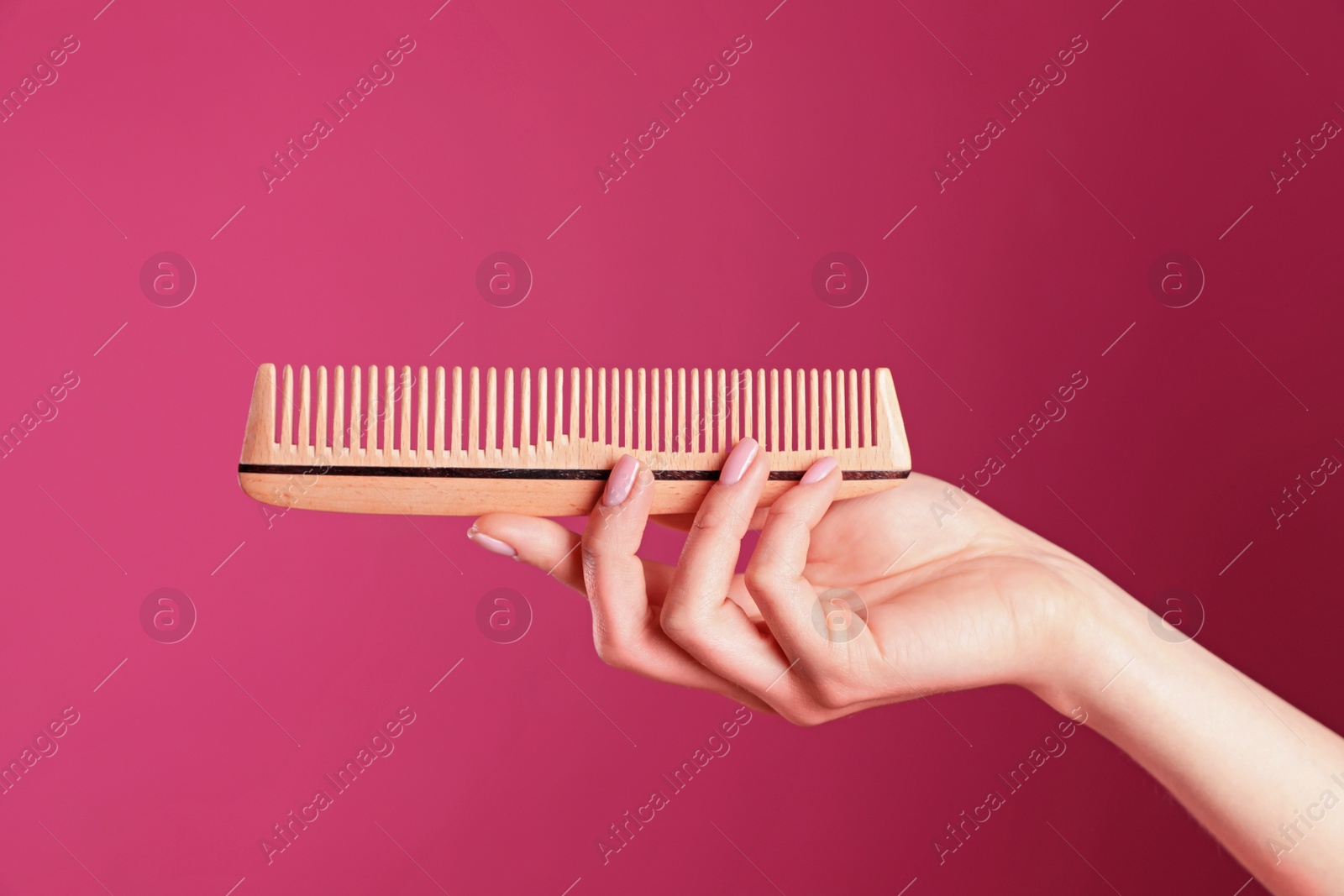 Photo of Woman holding wooden hair comb against crimson background, closeup