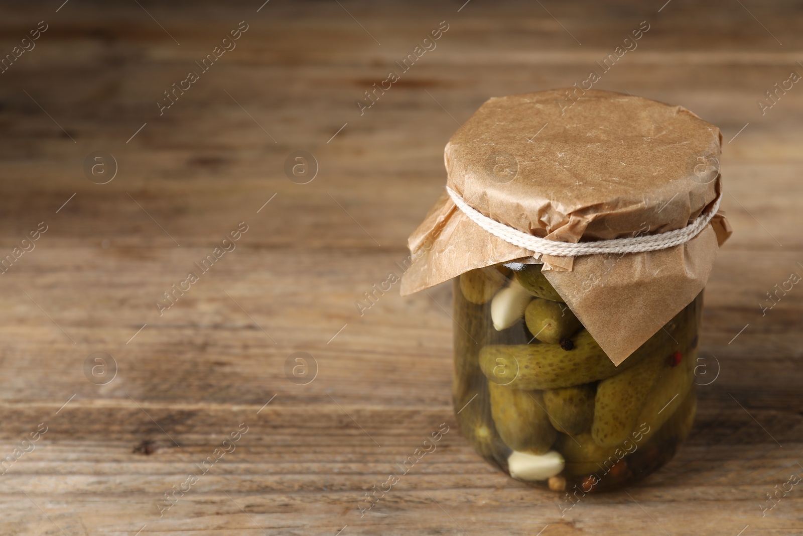 Photo of Tasty pickled cucumbers in glass jar on wooden table, space for text