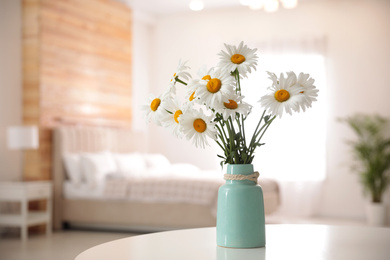 Beautiful bouquet of chamomile flowers in vase on white table indoors. Space for text