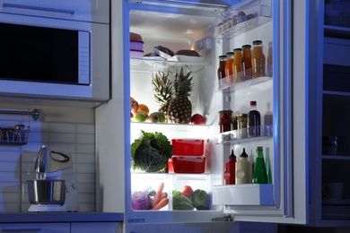 Photo of Open refrigerator full of products in stylish kitchen interior at night