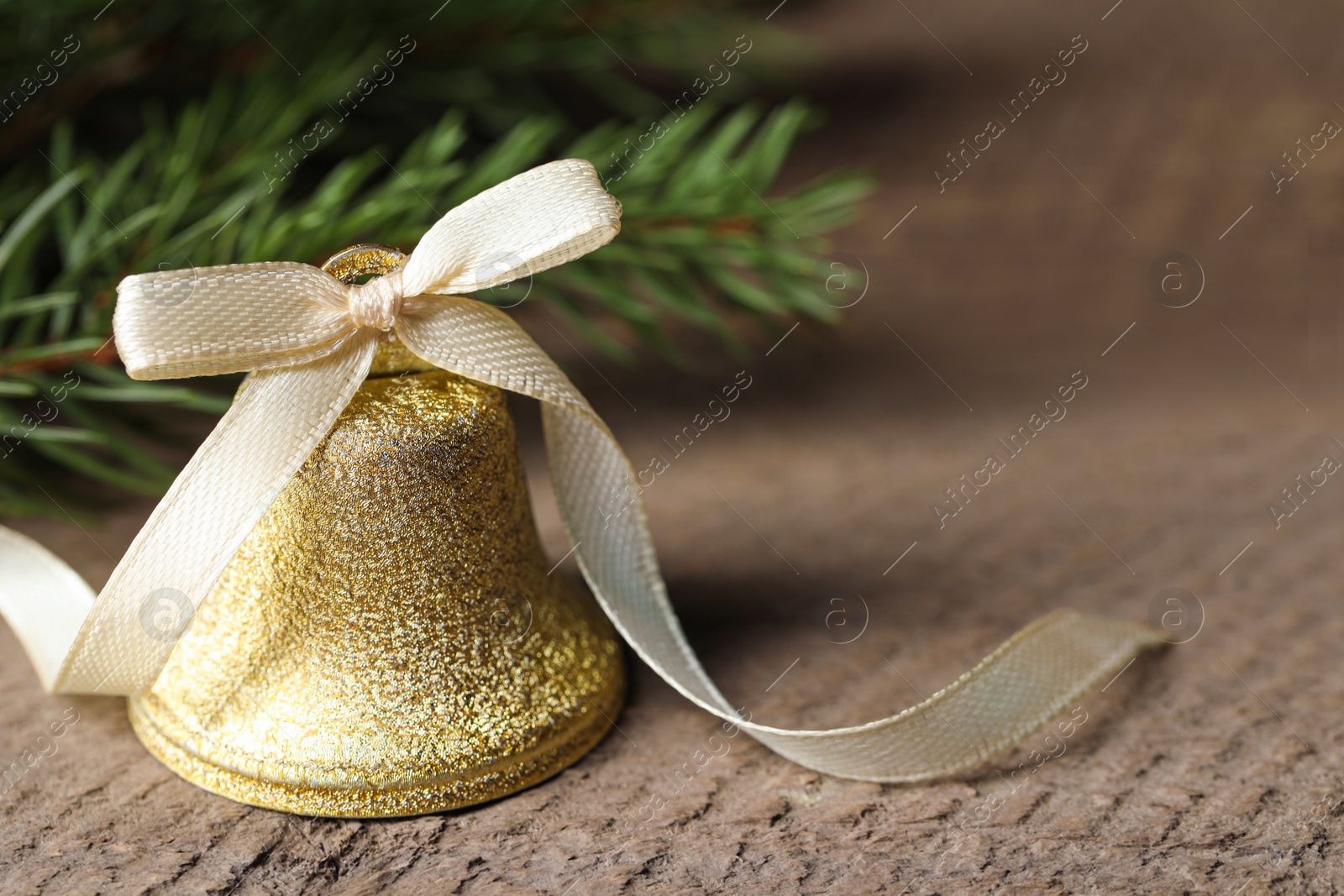 Photo of Bell and fir tree branches on wooden table, closeup with space for text. Christmas decor