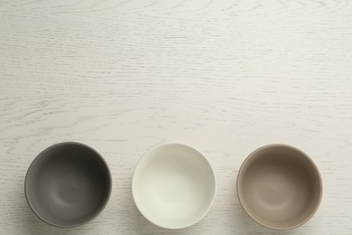 Stylish empty ceramic bowls on white wooden table, flat lay and space for text. Cooking utensils