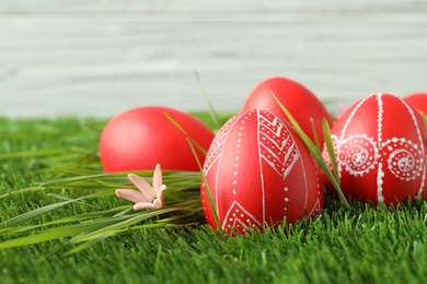 Photo of Red painted Easter eggs on green grass against light background. Space for text