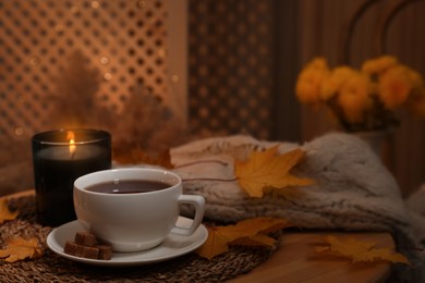 Cup of aromatic tea with sugar and autumn leaves on wooden table indoors, space for text