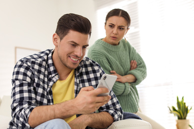 Photo of Distrustful woman peering into boyfriend's smartphone at home. Jealousy in relationship