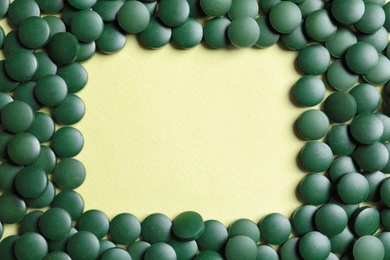 Photo of Frame made of green spirulina pills on color background, top view with space for text