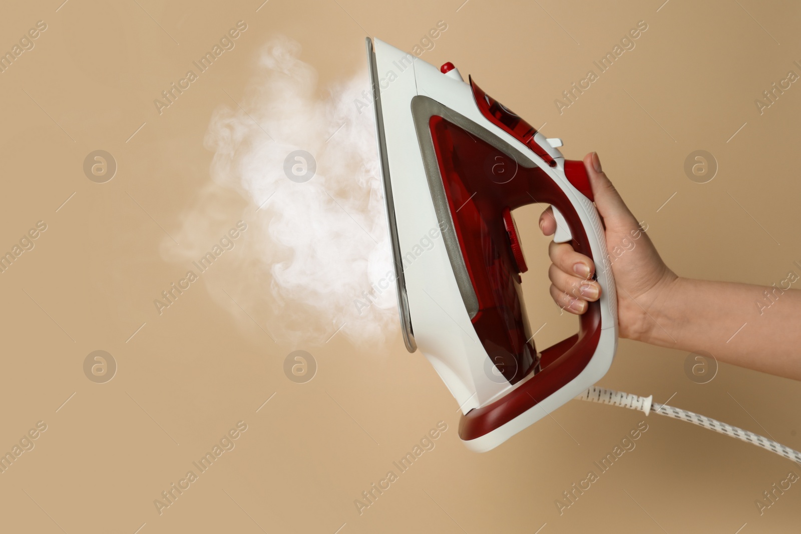 Image of Woman holding modern iron with steam on beige background, closeup. Space for text