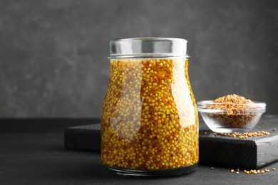 Photo of Whole grain mustard in jar and dry seeds on black wooden table