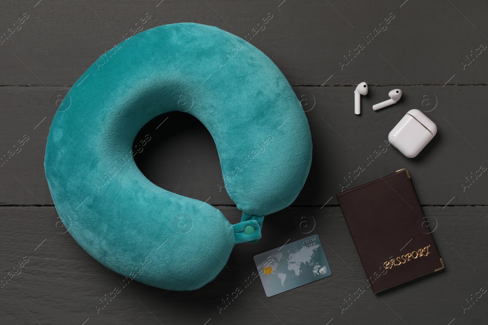 Photo of Turquoise travel pillow, passport, credit card and earphones on black wooden background, flat lay