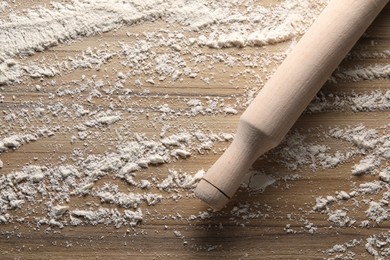 Photo of Scattered flour and rolling pin on wooden table, top view