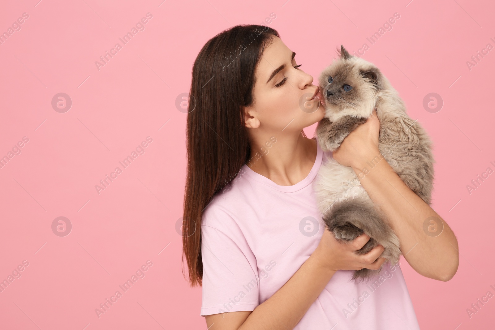 Photo of Woman kissing her cute cat on pink background, space for text