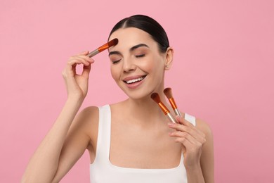 Happy woman with different makeup brushes on pink background