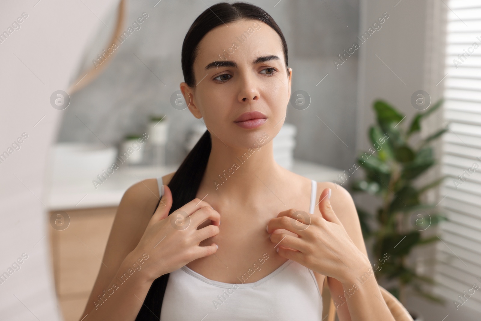 Photo of Woman with dry skin looking at mirror in bathroom