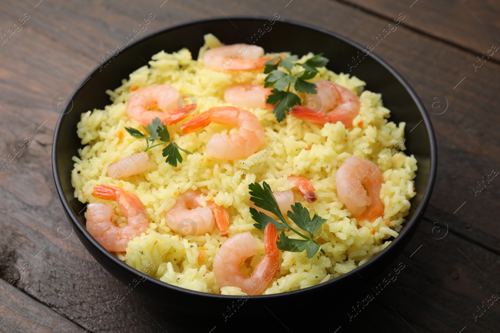 Photo of Delicious risotto with shrimps and parsley in bowl on wooden table, closeup