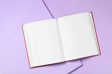 Photo of Open book with blank pages on violet background, top view. Space for text