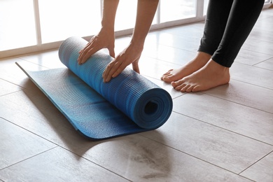 Woman rolling yoga mat on floor indoors, closeup