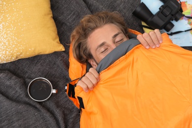 Young man in comfortable sleeping bag on blanket, top view