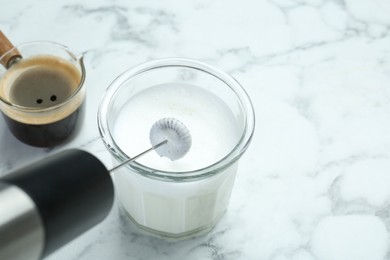 Mini mixer (milk frother), whipped milk in glass and coffee on white marble table, closeup. Space for text