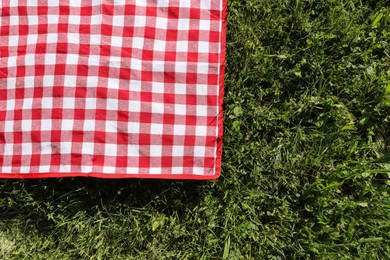 Photo of Checkered picnic tablecloth on fresh green grass, top view. Space for text