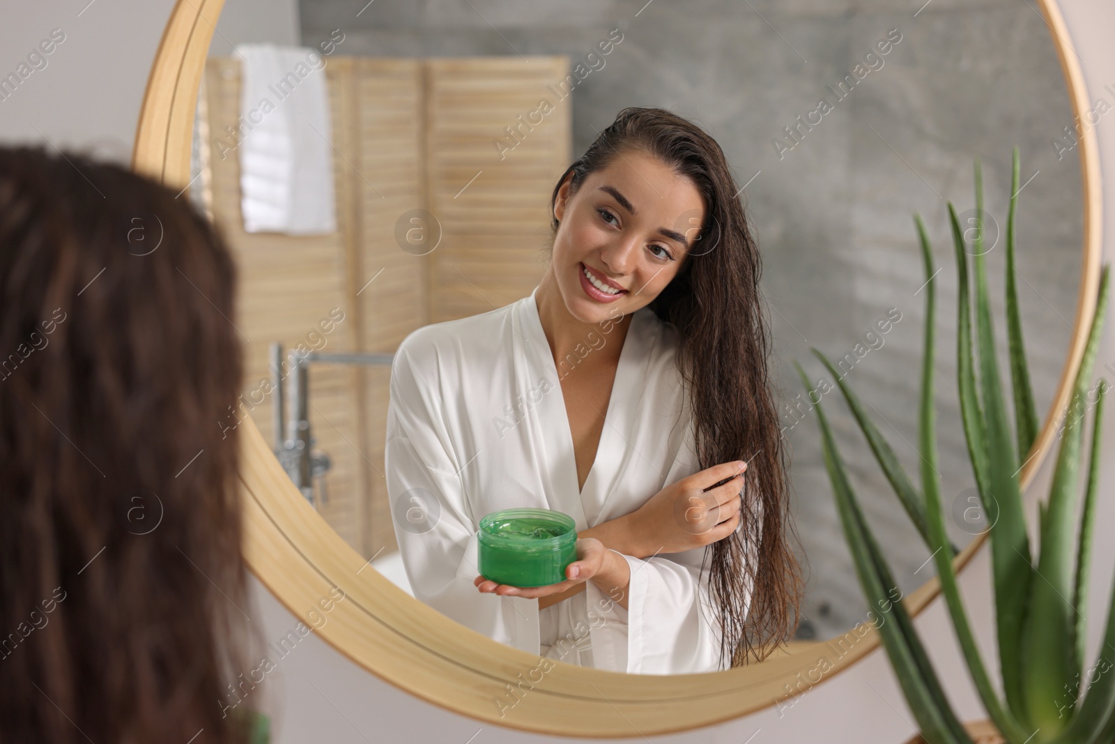 Photo of Young woman applying aloe hair mask near mirror in bathroom
