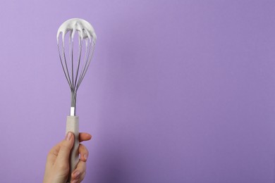 Photo of Woman holding whisk with whipped cream on violet background, closeup. Space for text