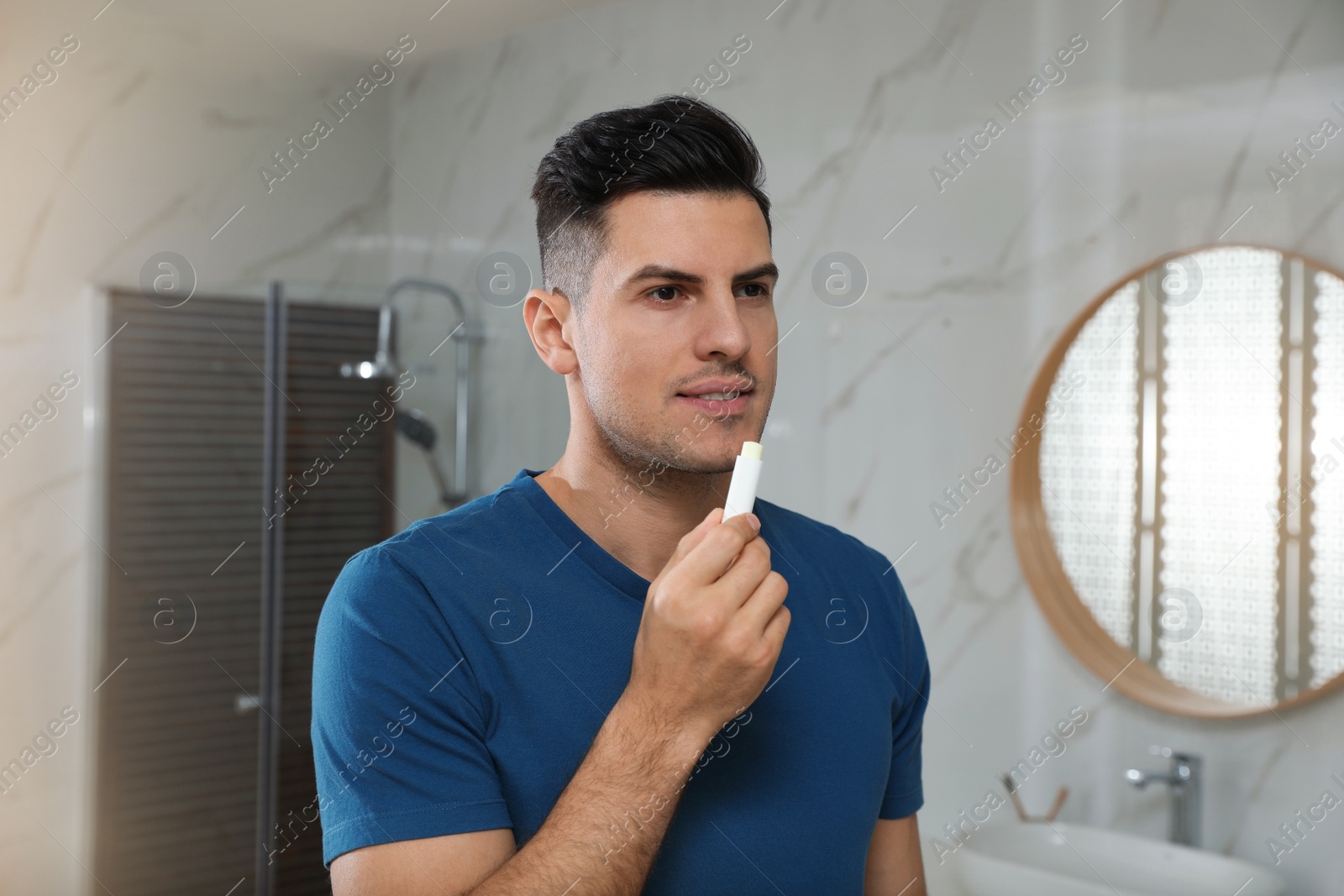 Photo of Man applying hygienic lip balm in bathroom